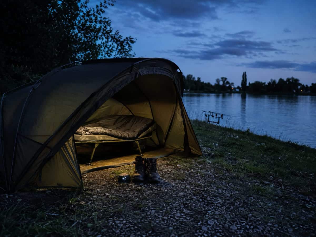 Bivvy ouvert avec bedchair et lampe frontale sur une berge au crépuscule