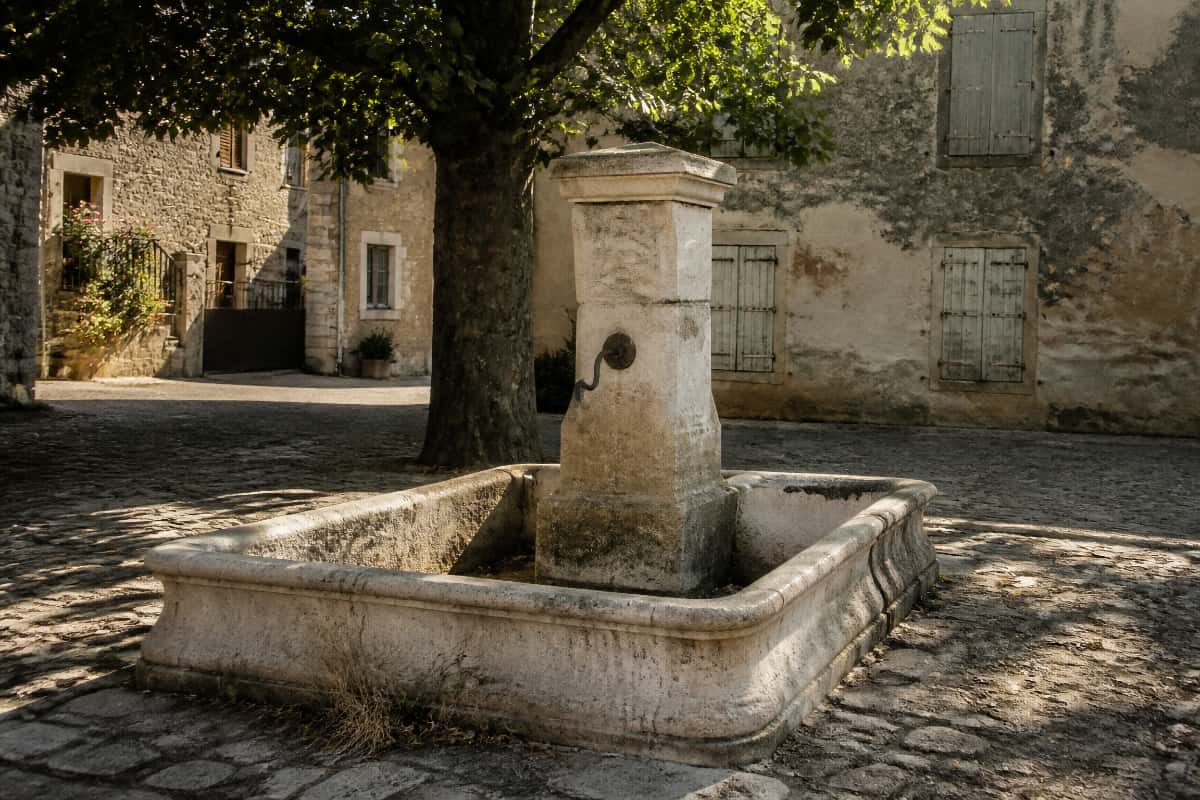 Fontaine de village sans eau sur une place ombragée, en période estivale