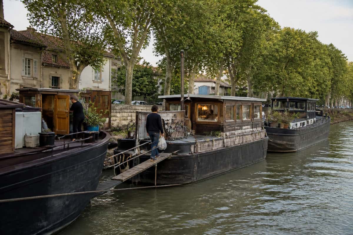 Plusieurs péniches-logements amarrées le long d’un quai de Saône, avec des habitants empruntant les passerelles